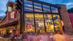 motion capture photo of people coming in and out of Sugarlands Distilling Co. with neon Moonshine sign showing through the buildings window at Gatlinburg, Tennessee, USA